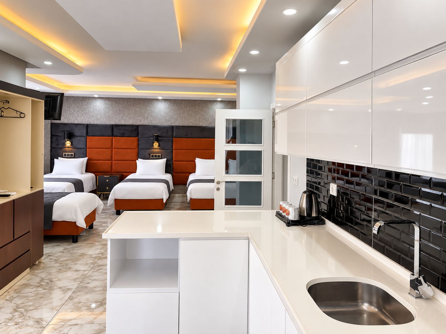 A hotel room with a modern design, featuring a large bed, a separate seating area, a kitchenette, and a bathroom.