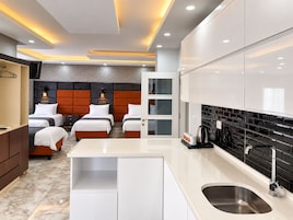 Habitación de hotel con diseño moderno, que incluye una cama grande, zona de estar separada, kitchenette y un baño.