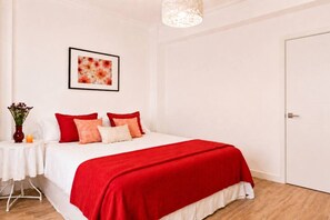 A hotel room with a bed, a framed picture on the wall, a nightstand with a vase and candle, and a door. - Cozy and spacious flat in the heart of Russafa (València)