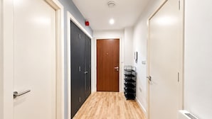 Un pasillo con suelo de madera, una puerta de madera al final y un estante metálico negro con repisas.
