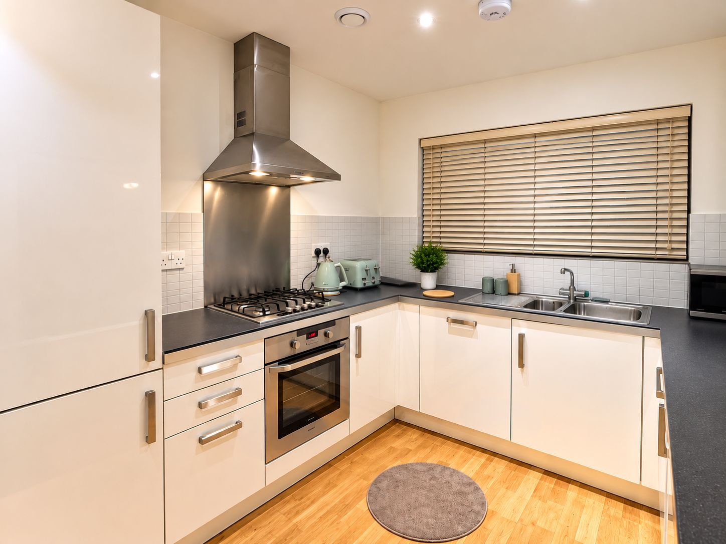 A modern kitchen with stainless steel appliances, a built-in oven, and a window with blinds.