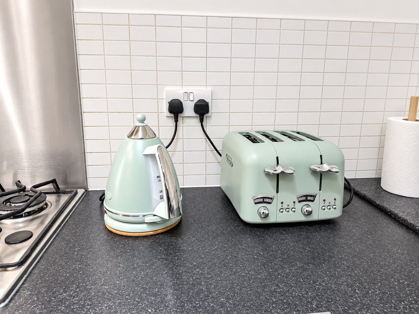 A kitchen with a gas stove, a kettle, and a vintage-style toaster on a black countertop.