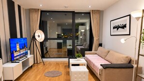 Een moderne woonkamer met een flatscreen televisie, een bank, een salontafel en een vloerlamp.