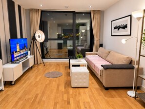 En moderne stue med et fladskærms-tv, en sofa, et sofabord og en gulvlampe.