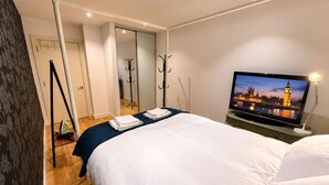 Een hotelkamer met een bed, een televisie waarop een stadsbeeld te zien is, een bureau met een lamp en een kapstok.