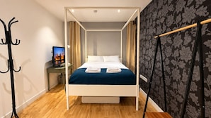 Un dormitorio moderno con cama a dosel, un televisor en una mesita de noche y un perchero.