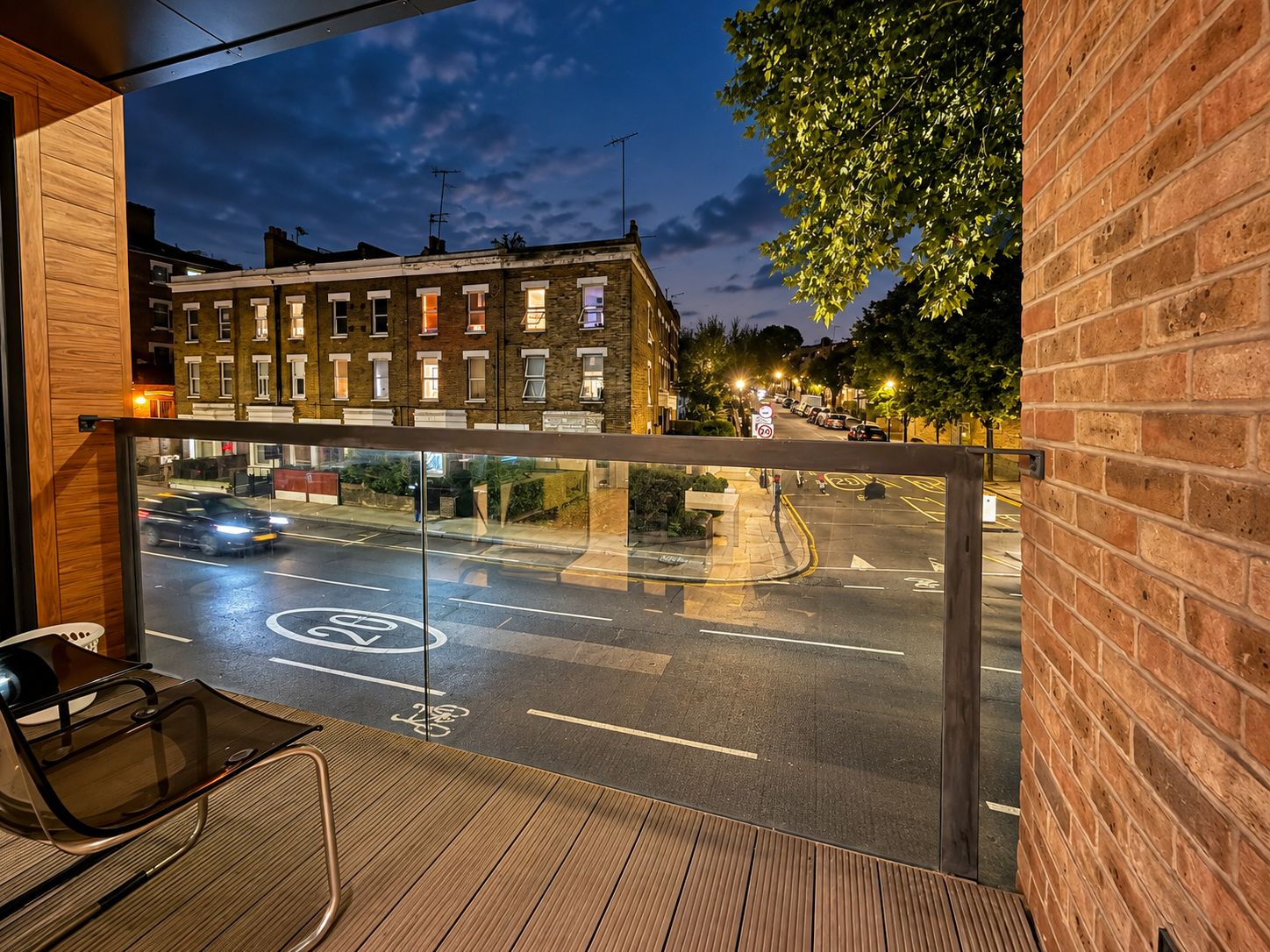 A balcony with a view of a street at night, including a brick building and parked cars.
