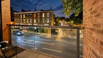 A balcony with a view of a street at night, including a brick building and parked cars.