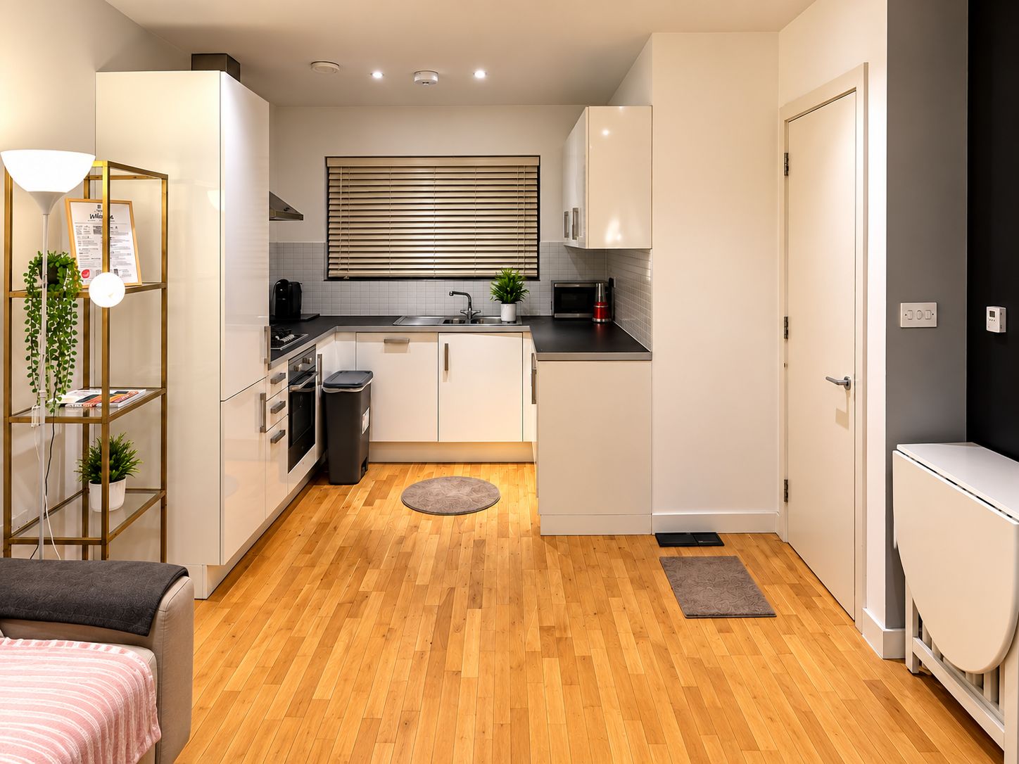 A compact kitchen with white cabinets, a black countertop, and a window with blinds.