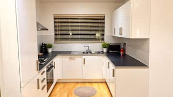 Una cocina moderna con armarios blancos, encimera negra, pileta de acero inoxidable, ventana con persianas y piso de madera.