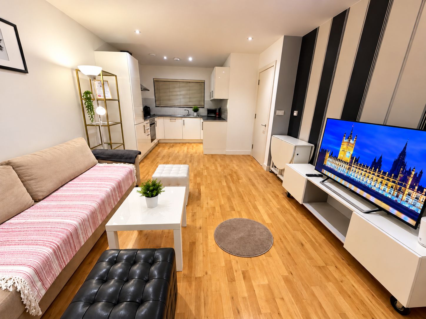 Una sala moderna con un sofá, una mesa de centro, un televisor y una cocina al fondo.