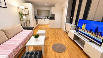Una sala moderna con un sofá, una mesa de centro, un televisor y una cocina al fondo.