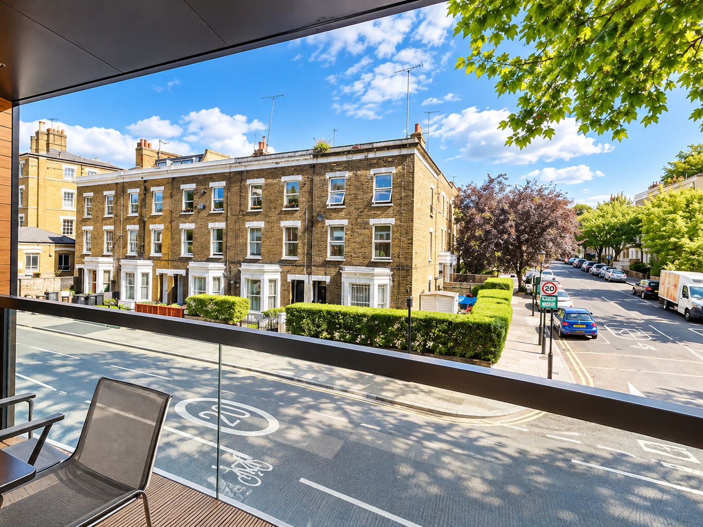A view from a window overlooking a street with a row of terraced houses, a designated bike lane, and parked cars.