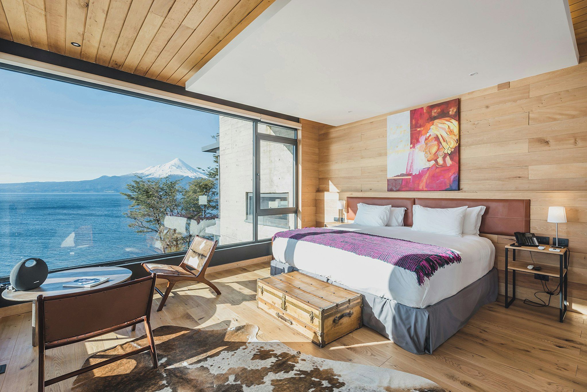 A modern bedroom with a large window, a bed, a desk, and a view of a mountain.