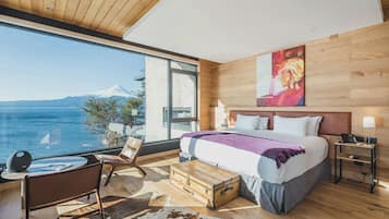 A modern bedroom with a large window, a bed, a desk, and a view of a mountain.