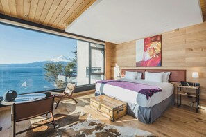 A modern bedroom with a large window, a bed, a desk, and a view of a mountain. - Hotel Awa (Puerto Varas)