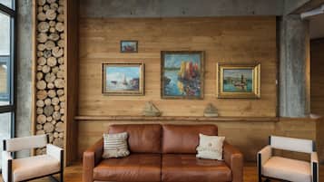 A room with a brown leather sofa, two armchairs, and three framed paintings on the wall.
