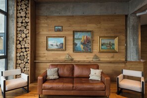 A room with a brown leather sofa, two armchairs, and three framed paintings on the wall. - Hotel Awa (Puerto Varas)