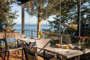 An outdoor dining area with a table set for two, overlooking a body of water and trees. - Hotel Awa (Puerto Varas)