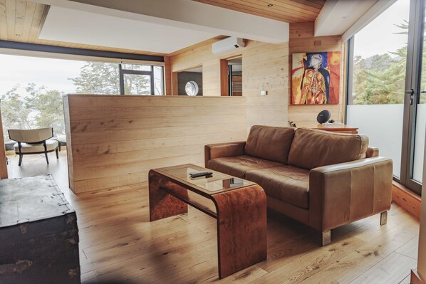 A modern living room with a brown leather sofa, a glass coffee table, and a wooden floor. - Hotel Awa (Puerto Varas)