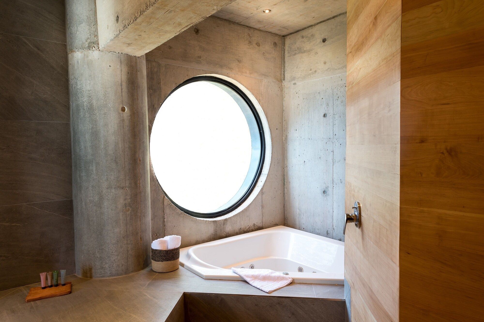 A bathroom with a bathtub, a round window, and a wooden door.