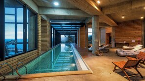 A long indoor swimming pool with clear glass walls, wooden paneling, and lounge chairs along the side. - Hotel Awa (Puerto Varas)