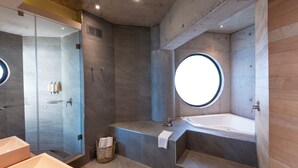 Een moderne badkamer met een ruime badkuip, een inloopdouche en een rond raam.