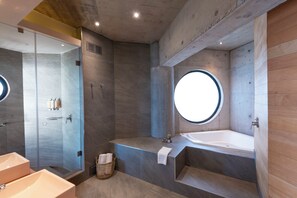 A modern bathroom with a large bathtub, a walk-in shower, and a round window. - Hotel Awa (Puerto Varas)
