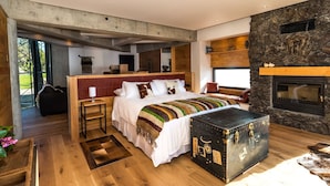 A modern bedroom with a large bed, a stone fireplace, and a view of the outdoors. - Hotel Awa (Puerto Varas)