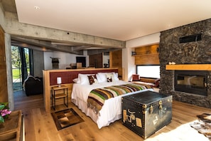 A modern bedroom with a large bed, a stone fireplace, and a view of the outdoors. - Hotel Awa (Puerto Varas)
