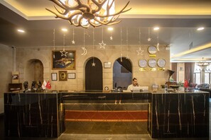 A hotel reception area with a marble counter, a chandelier, framed pictures, and clocks displaying different cities. - Buyuk Mardin (Mardin)
