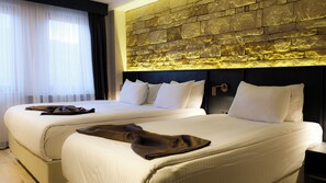 A hotel room with two beds, a stone accent wall, and a window with sheer curtains. - Buyuk Mardin (Mardin)