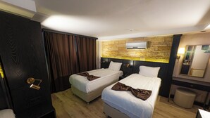 Ein Hotelzimmer mit zwei Betten, Holzboden, einer Wand mit Steinverkleidung, einer schwarzen Tür und einem Spiegel.