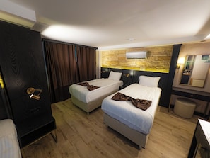 Ein Hotelzimmer mit zwei Betten, Holzboden, einer Wand mit Steinverkleidung, einer schwarzen Tür und einem Spiegel.