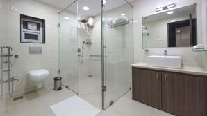 Un baño moderno con ducha envuelta en vidrio, lavamanos blanco y tocador de madera.