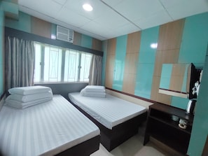 A hotel room with two beds, a window with curtains, a wall-mounted TV, and a small shelf with a kettle.