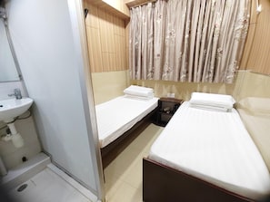 A small, compact hotel room with two single beds, a sink, and a mirror.
