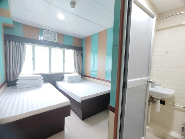 A hotel room with two beds, a window with curtains, a sink, and a shower area.