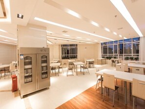 A modern dining area with tables and chairs, a refrigerator, and large windows. - Greentree INN Zhangjiakou High Speed Railway Station (Zhangjiakou)
