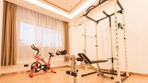 Een sportschool met trainingsapparatuur, waaronder een rode hometrainer, een bank en een squatrek.
