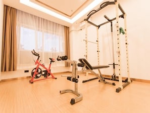 Ein Fitnessraum mit Trainingsgeräten, darunter ein rotes Ergometer, eine Bank und ein Squat-Gestell.