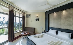 A hotel room with a bed, a chair, a small table, and a large window. - Hotel Sonar Bangla Mandarmoni (Kanthi)