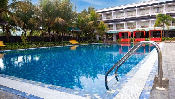 Une piscine à l’eau d’un bleu cristallin, entourée de palmiers et bordée d’un hôtel doté de nombreux balcons.