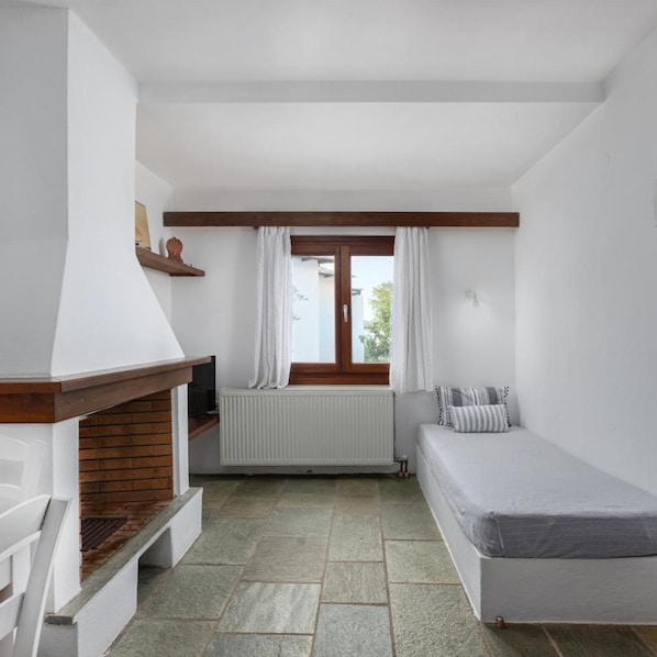 Una habitación pequeña y limpia con una cama, un radiador, una ventana con cortinas y un techo con vigas de madera.