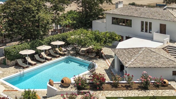 Ein Poolbereich mit Liegestühlen und Sonnenschirmen, ein weißes Gebäude mit einem Ziegeldach und Blick auf das Meer.