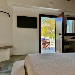 Un dormitorio con cama, televisor montado en la pared y puerta que da a un área de estar exterior con mesa y sillas.