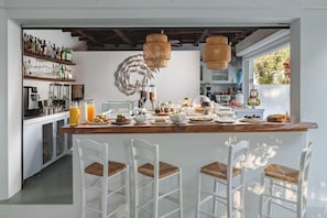 Una cocina con barra, taburetes blancos y una variedad de alimentos y bebidas.