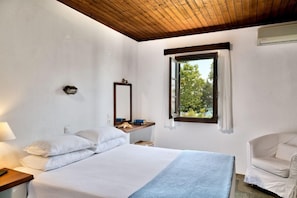 Un dormitorio con cama, mesita de noche, silla, ventana y espejo.