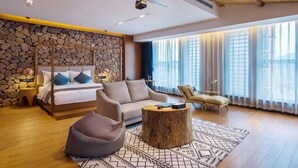 Ein modernes Schlafzimmer mit Steinwand, einem Bett, einer Couch, einem Couchtisch und Blick ins Freie.