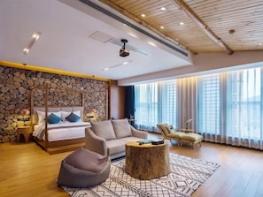 Une chambre moderne avec un mur en pierre, un lit, un canapé, une table basse et une vue sur l’extérieur.